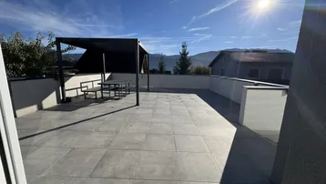 Weitläufige Sonnenterrasse mit Pergola und Essbereich, bietet einen schönen Blick auf die Berge.