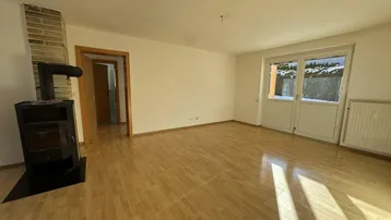Helles Wohnzimmer mit Laminatboden, Kaminofen und Zugang zur Terrasse.