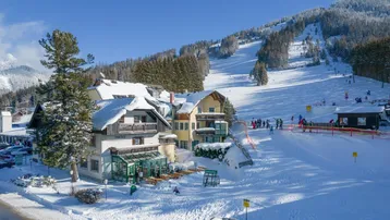Hotelgebäude im Winter mit verschneiten Dächern und direktem Zugang zu den Skipisten.