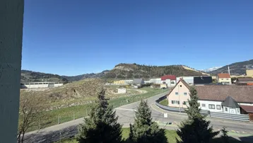 Weitläufiger Blick auf die umliegende Berglandschaft und grüne Hügel unter blauem Himmel.