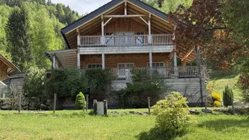 Charmantes Holzhaus mit Balkonen und Garten in einer grünen, bergigen Umgebung.