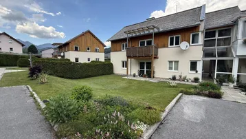 Mehrfamilienhaus mit Holzfassade, Balkonen und gepflegtem Vorgarten in ländlicher Umgebung.