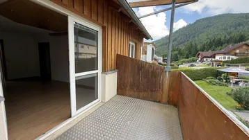 Heller Balkon mit Holzwänden, Metallboden und weitem Blick auf die Berge und grüne Landschaft.