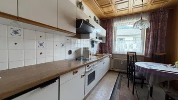 Funktionale Küche mit weißen Schränken, Holzarbeitsplatte und Essbereich.