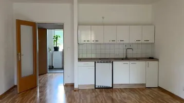 Heller Wohnbereich mit integrierter Küchenzeile, Parkettboden und Zugang zu weiteren Räumen.
