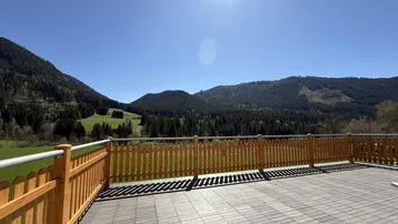 Große Terrasse mit Holzzaun und weitem Blick auf die umliegende Berglandschaft unter blauem Himmel.