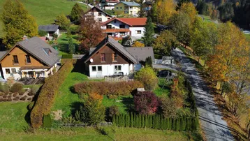 Luftaufnahme eines Einfamilienhauses mit gepflegtem Garten und umliegender Natur im Herbst.