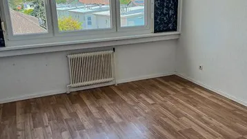 Helles Zimmer mit Laminatboden und Fensterblick auf die Umgebung, ideal als Schlafzimmer nutzbar.