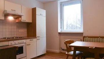 Helle Küche mit Einbauküche, Essbereich und Fensterblick ins Freie.