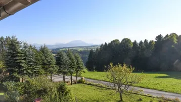 Weitläufiger Blick vom Balkon über grüne Wiesen und Wälder bis zu den fernen Bergen.