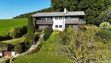 Malerisches Einfamilienhaus in Hanglage, umgeben von einem gepflegten Garten und grüner Natur.