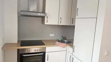 Kleine, funktionale Küche mit weißen Schränken, Holzarbeitsplatte und integrierten Geräten.