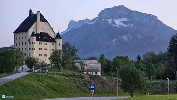 Historisches Gebäude mit imposanter Architektur vor einer malerischen Bergkulisse und grüner Umgebung.