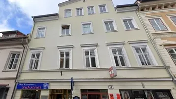 Historisches Gebäude mit mehreren Etagen und Geschäften im Erdgeschoss an einer belebten Straße.
