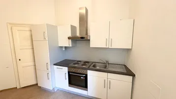 Kleine, funktionale Küche mit weißen Schränken, Spüle, Kochfeld und Dunstabzugshaube.