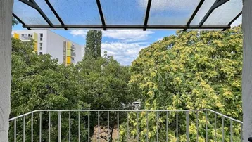 Überdachter Balkon mit Metallgeländer und Blick ins Grüne sowie auf umliegende Gebäude.