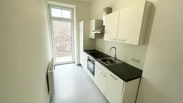 Funktionale Küchenzeile mit weißen Schränken, dunkler Arbeitsplatte und Zugang zum Balkon.