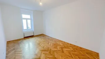 Heller Raum mit Fischgrätparkettboden und einem Fenster, ideal als Wohn- oder Schlafzimmer.