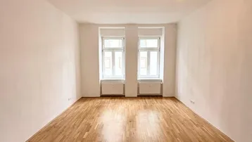 Helles Zimmer mit Holzboden und zwei großen Fenstern, bereit zur individuellen Gestaltung.