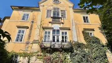 Historische Villa mit verwitterter Fassade, umgeben von üppigem Grün und Kletterpflanzen.