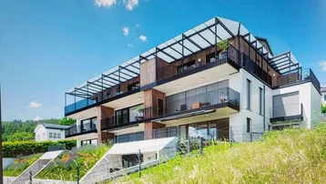 Moderne Wohnanlage mit mehreren Balkonen und Terrassen, eingebettet in eine grüne Hanglage.