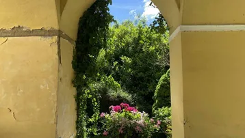 Blick durch einen historischen Bogen in einen grünen Garten mit blühenden Blumen und üppiger Vegetation.