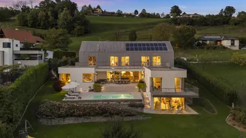 Moderne Villa mit Pool, großer Terrasse und weitläufigem Garten bei Sonnenuntergang.