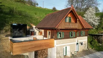 Traditionelles Holzhaus mit modernem Anbau und Holzlager am Hang gelegen.