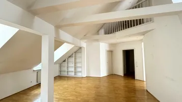 Geräumiger Wohnbereich im Dachgeschoss mit Holzbalken, Parkettboden und integriertem Regal.