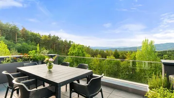 Große Dachterrasse mit Esstisch, Glasgeländer und weitem Blick über Wälder und Berge.
