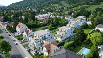 Luftaufnahme einer modernen Wohnanlage mit mehreren Gebäuden, umgeben von viel Grün und Weinbergen.