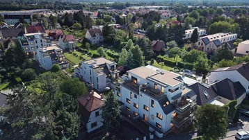 Luftaufnahme einer modernen Wohnanlage in grüner Umgebung mit Bergblick und umliegenden Häusern.