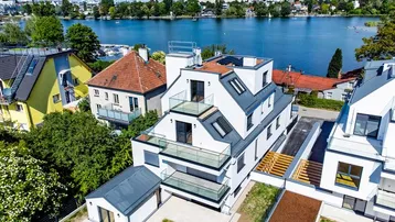 Moderne Wohnanlage am Seeufer mit mehreren Gebäuden, Grünflächen und Photovoltaikanlage auf dem Dach.