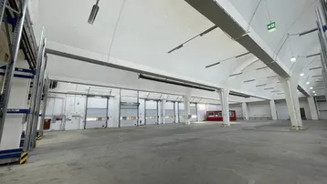 Große, leere Lagerhalle mit hohen Decken, Betonboden und mehreren Rolltoren für den Zugang.