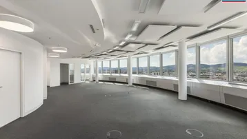 Großes, leeres Büro mit Teppichboden und vielen Fenstern, die eine weite Aussicht auf die Stadt bieten.