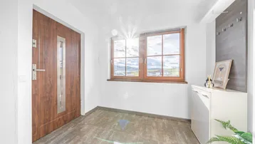 Heller Eingangsbereich mit Fliesenboden, Holztür und Fenster mit Weitblick.