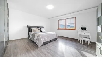 Helles Schlafzimmer mit Holzboden, großem Fenster und Bergblick.