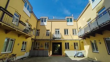 Innenhof eines Wohngebäudes mit gelben Fassaden, gepflastertem Boden und Balkonen.