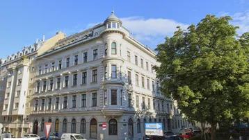 Historisches Eckgebäude mit klassischer Architektur und vielen Fenstern an einem sonnigen Tag.