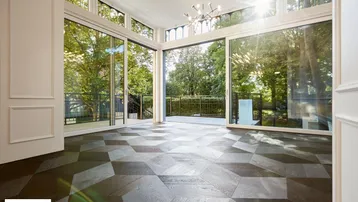 Helles Wohnzimmer mit großen Fenstern, Parkettboden und Zugang zu einem Balkon mit Blick ins Grüne.