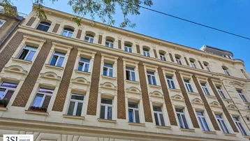 Detailansicht der historischen Fassade mit verzierten Fenstern und Balkonkästen unter blauem Himmel.