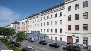 Ansicht der Wohnhausfassade mit mehreren Stockwerken und parkenden Autos auf der Straße.
