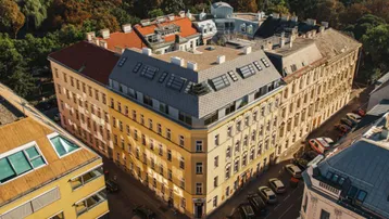 Luftaufnahme eines historischen Wohngebäudes mit modernisiertem Dachgeschoss und umliegender Grünfläche.