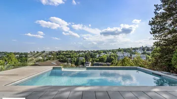Moderner Außenpool mit Infinity-Effekt und weitem Blick über die Stadt und grüne Landschaft.