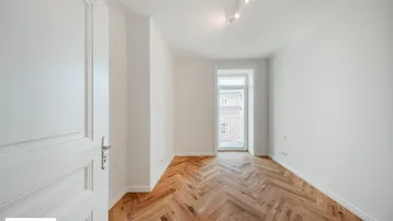 Lichtdurchfluteter Raum mit Fischgrätparkett und Zugang zu einem französischen Balkon.