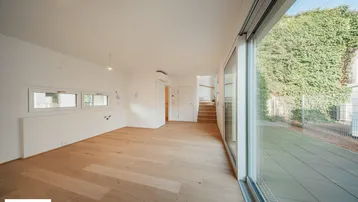 Heller, leerer Raum mit Holzboden und großen Fenstern, die Zugang zu einer Terrasse bieten.