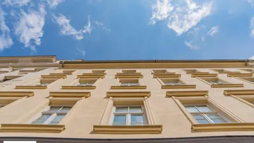 Blick nach oben auf die Fassade eines Altbaus mit vielen Fenstern unter einem blauen Himmel mit Wolken.