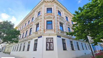 Historisches Eckgebäude mit eleganter Fassade und vielen Fenstern unter blauem Himmel.