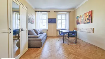 Helles Wohnzimmer mit Schlafsofa, Esstisch und elegantem Fischgrätparkettboden.