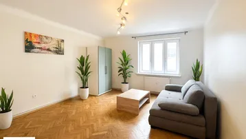 Helles Wohnzimmer mit Fischgrätparkett, einem Sofa und dekorativen Pflanzen.
